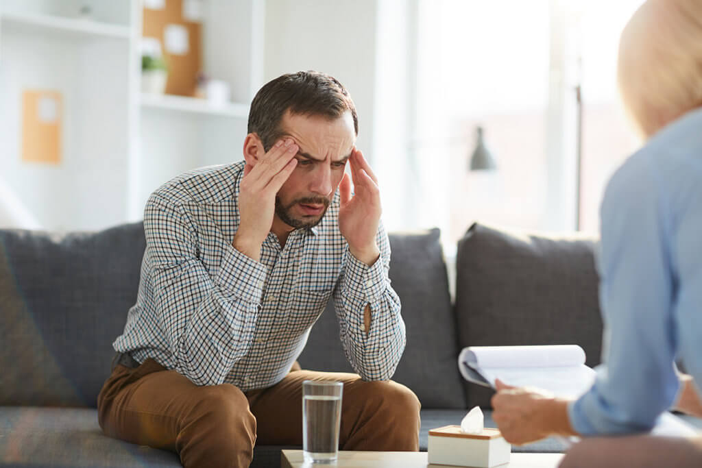 man holds his head and talks to female therapist about psychological dependence
