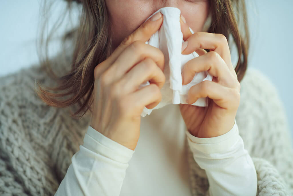 woman blowing her nose due to a compromised immune system