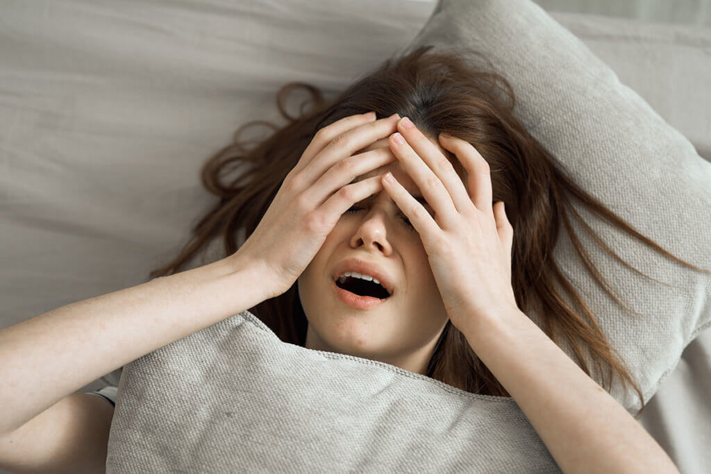 woman in bed with hands over face shocked after learning what is codependency
